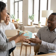 Une femme offre un cadeau à un collègue souriant dans un bureau moderne. Le geste symbolise le bien-être et la reconnaissance.