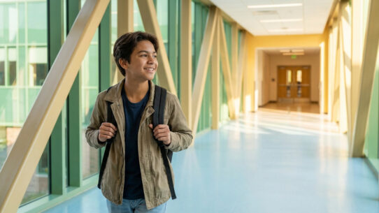 Jeune lycéen souriant avec un sac à dos, marchant dans un couloir moderne et lumineux, symbolisant un transfert réussi.
