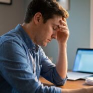 Un homme fatigué tenant sa tête dans sa main devant son ordinateur portable.