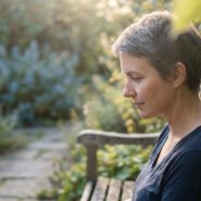 Femme pensive assise seule sur un banc de jardin, baignée dans une douce lumière dorée au crépuscule.