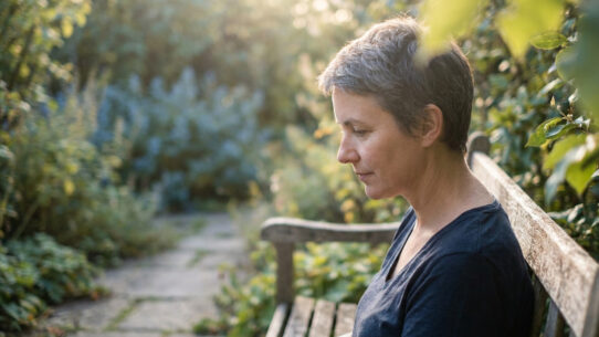 Femme pensive assise seule sur un banc de jardin, baignée dans une douce lumière dorée au crépuscule.