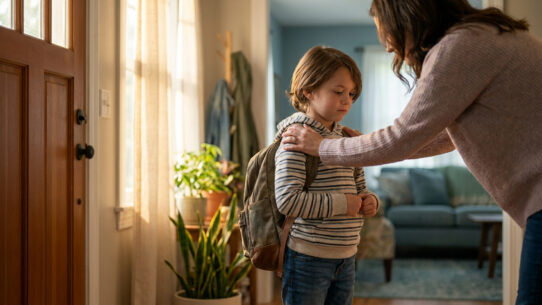 Une mère réconforte son jeune fils avec un sac à dos avant qu'il ne parte à l'école, près d'une porte d'entrée.