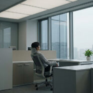 Employé de bureau assis seul dans un espace de travail calme, regardant par la fenêtre avec un air pensif.