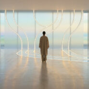 Une personne debout face à un mur lumineux épuré dans un espace minimaliste, symbolisant la sérénité et le calme.