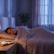 Une femme dort paisiblement dans un lit éclairé par une lampe de chevet douce.