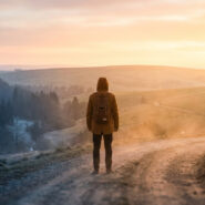Une personne avec un sac à dos marchant sur un chemin de terre vers un paysage ensoleillé.