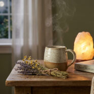 Une tasse de tisane fumante, un bouquet de fleurs séchées et une lampe de sel sur une table de chevet la nuit.